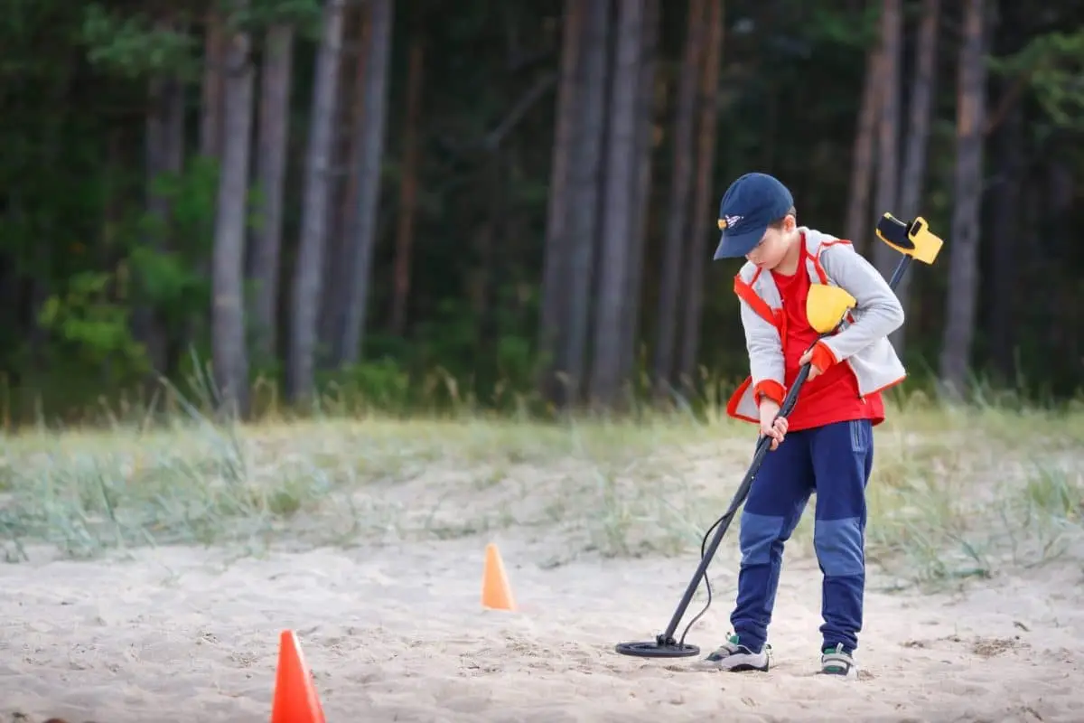 A photo of a child using a metal detector with orange cones around